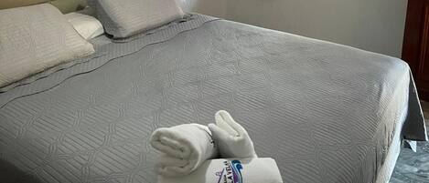 A hotel room with a bed, a painting on the wall, a window with curtains, and a bottle on the door.