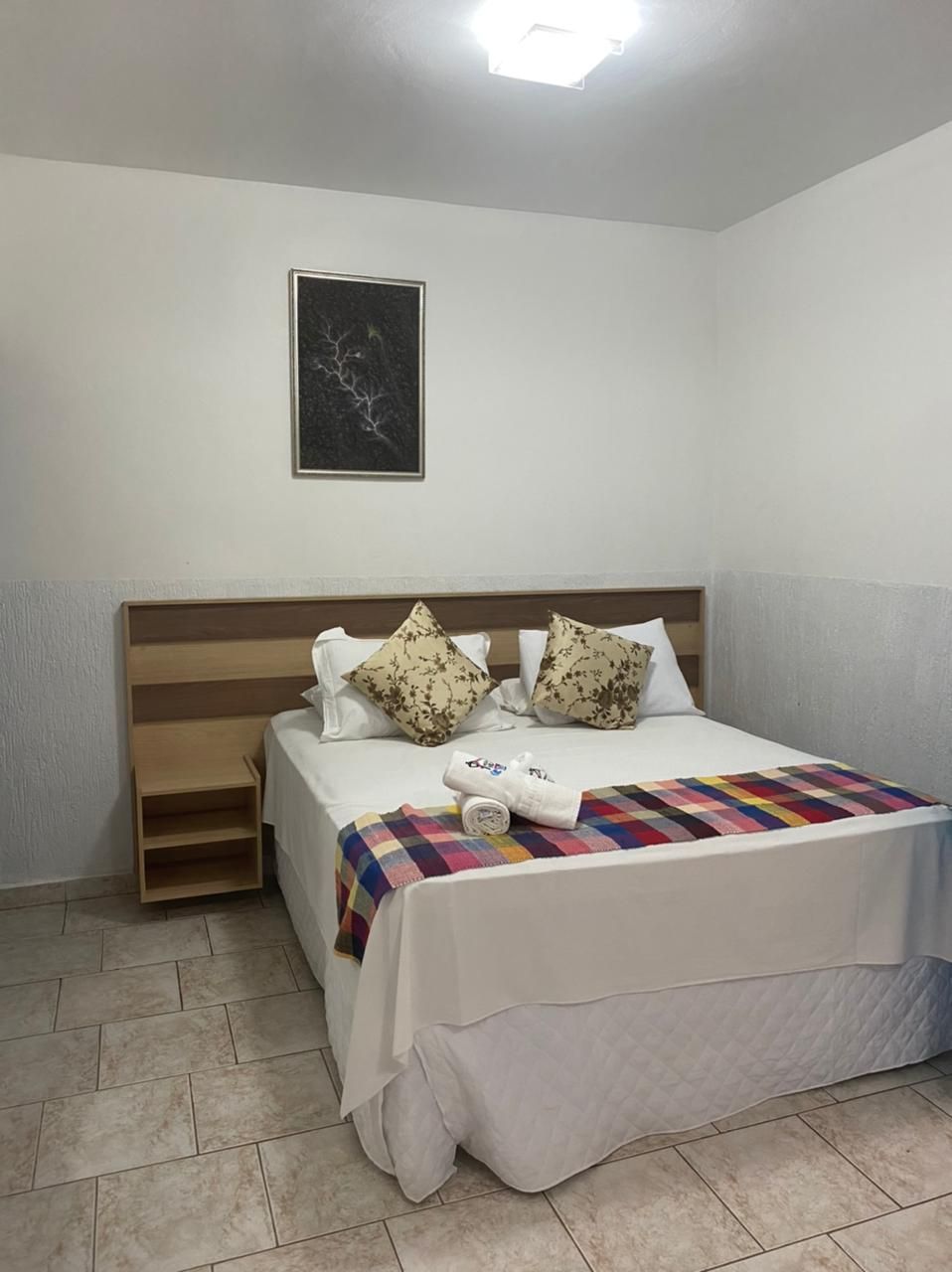 A single bed with a wooden headboard, a quilted mattress cover, and two pillows with a floral pattern.