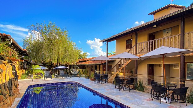 A swimming pool with tiled edges, outdoor seating, and a building with a balcony.