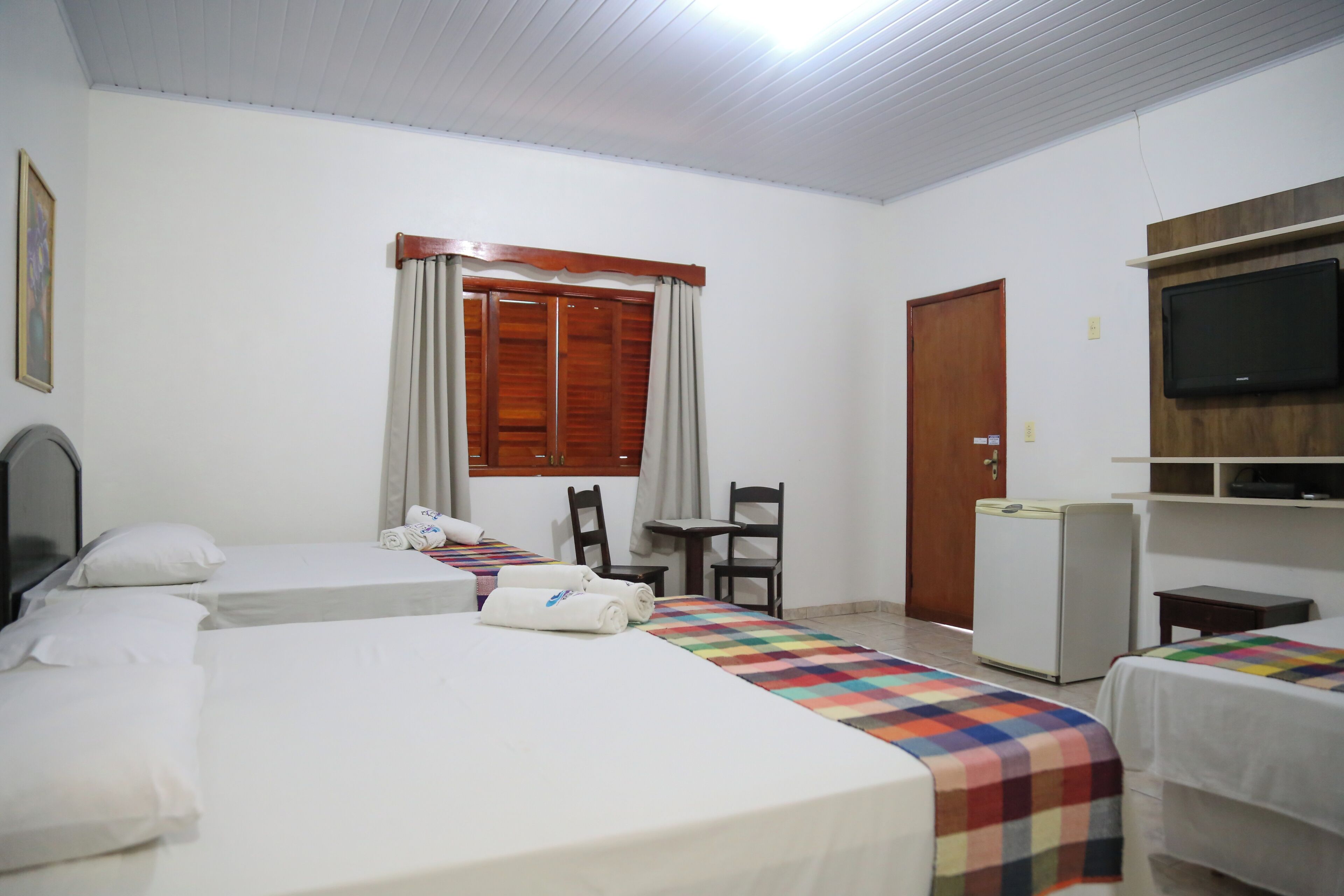 Une chambre d’hôtel avec deux lits simples, une petite table, une chaise, un téléviseur et une armoire.