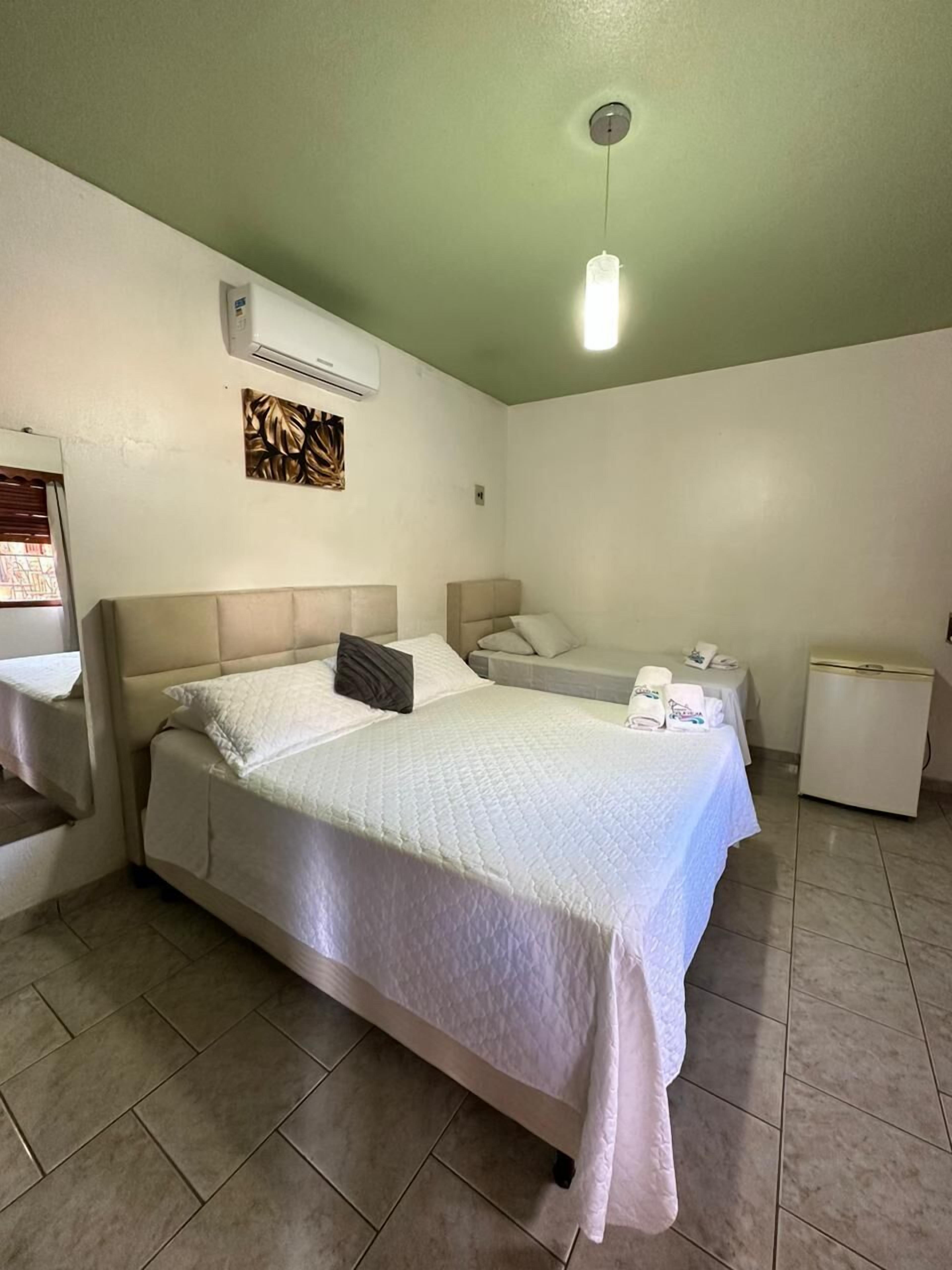 Habitación de hotel con cama, mesitas de noche, aire acondicionado de pared y lámpara colgante.