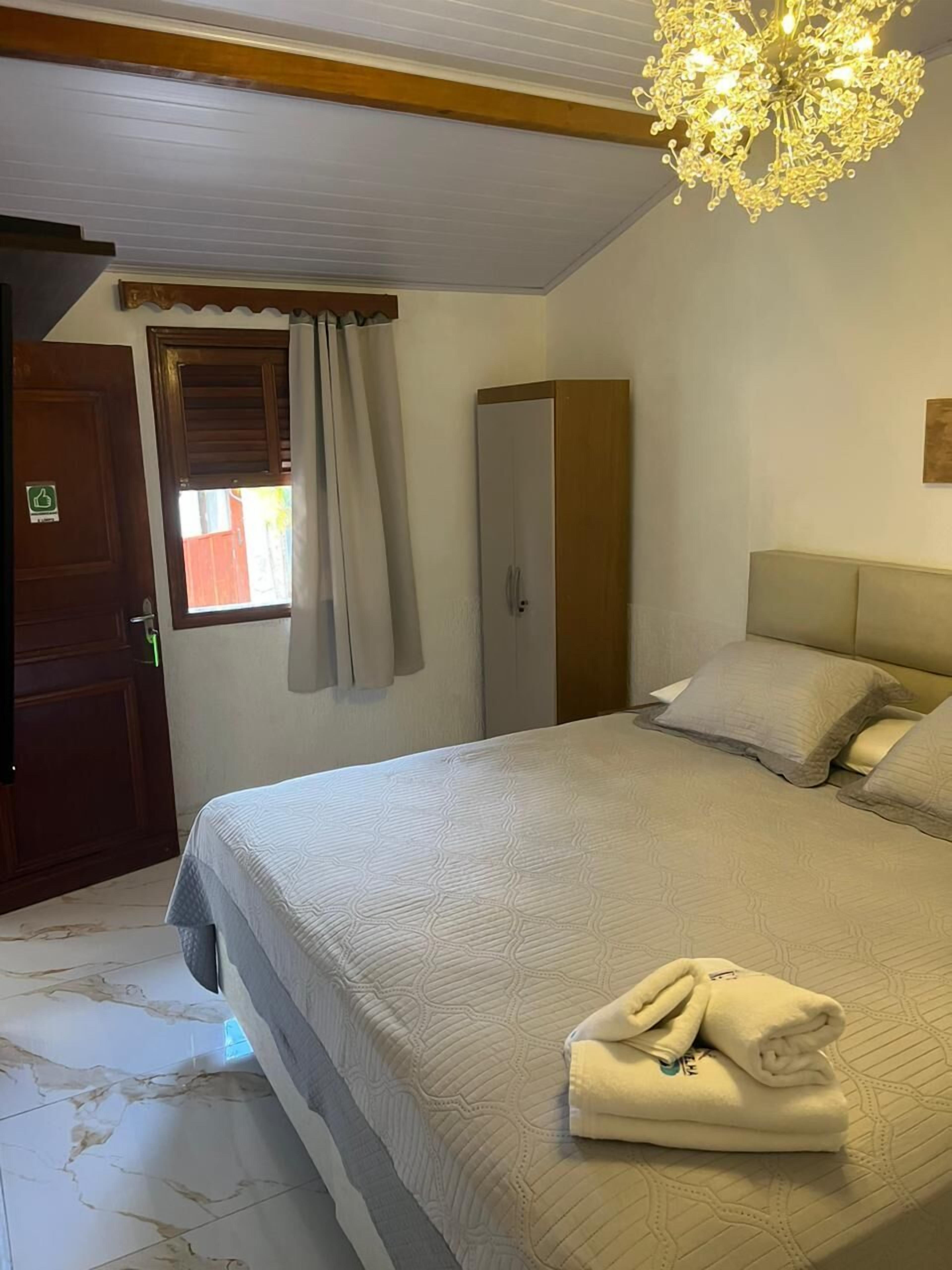 A hotel room with a bed, a wardrobe, a chandelier, and a window with curtains.