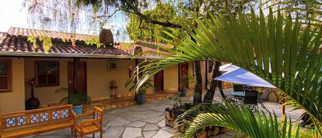 A courtyard with stone flooring, wooden benches, and potted plants.