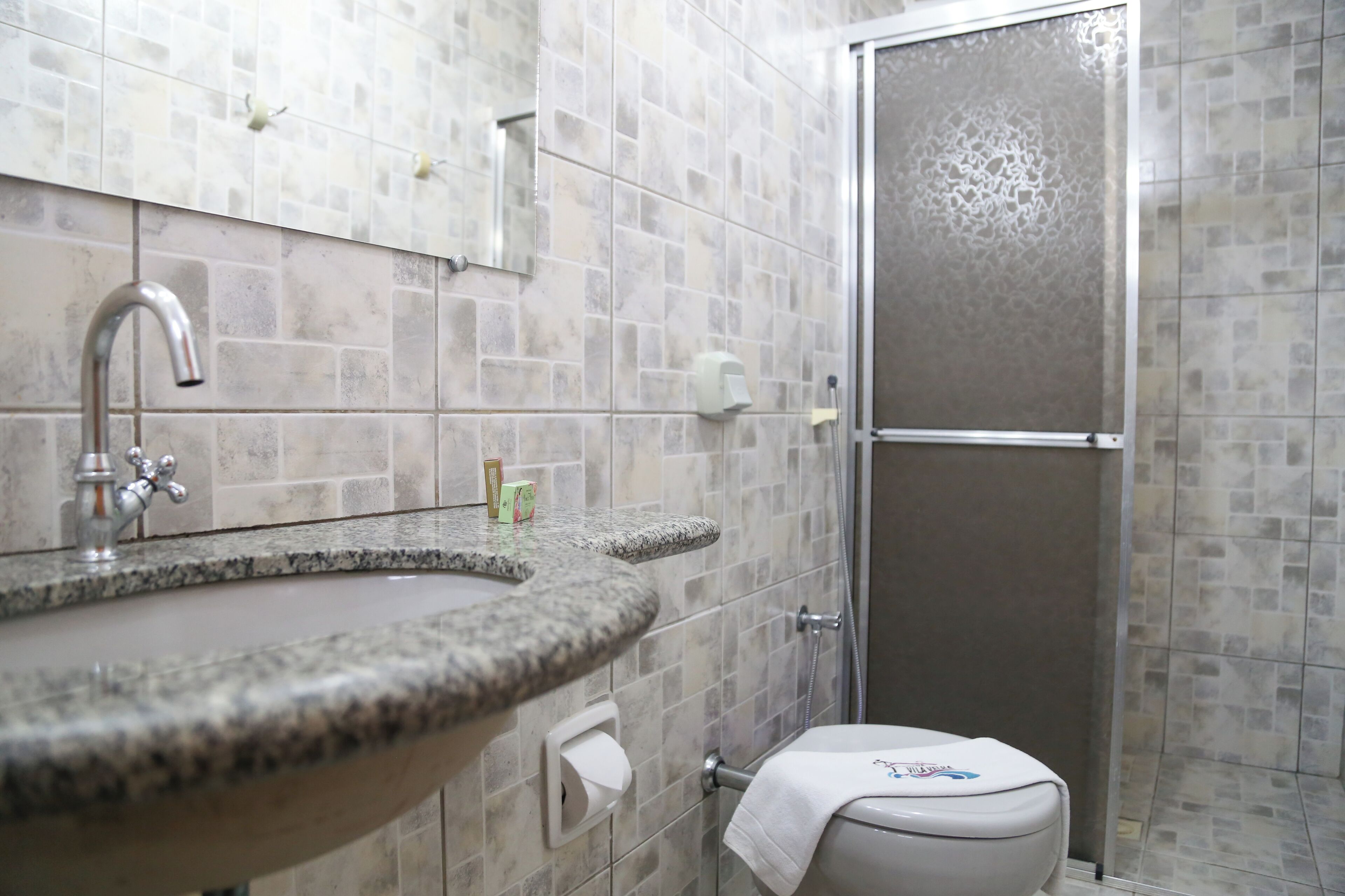 Ein Badezimmer mit einem Granitwaschbecken, einer Toilette und einer Duschkabine aus Glas.