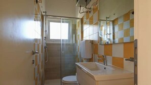Ein Badezimmer mit Duschkabine aus Glas, Toilette und Waschbecken mit Spiegel.