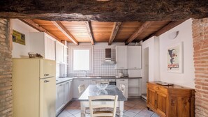 A kitchen with a tiled floor, wooden ceiling beams, a white refrigerator, a wooden cabinet, and a dining table with chairs. - Appartamento San Martino by Wonderful Italy (Bologna)