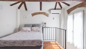 A bedroom with a bed, a curved brick wall, a window with curtains, and a wooden floor. - Appartamento San Martino by Wonderful Italy (Bologna)