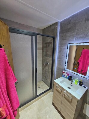 Bathroom features a glass-enclosed shower, vanity with sink, and mirror.