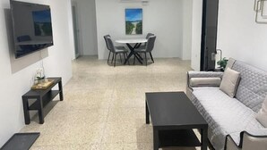 A modern living room with a sofa, a coffee table, a TV, and a dining area with a table and chairs. - Isla Verde Casa Azul (Isla Verde)