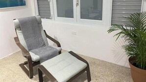A room with a large window, a chair, a small table, and a potted plant. - Isla Verde Casa Azul (Isla Verde)
