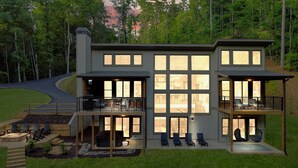 Uma casa moderna de dois andares com janelas amplas, um deck com área de estar externa e um caminho de pedra que leva à entrada.