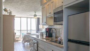 Eine moderne Küche mit weißen Schränken, einem Edelstahl-Kühlschrank und einem großen Fenster mit Blick auf einen Balkon.