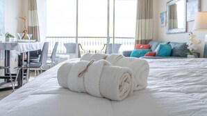 Et hotelværelse med en stor seng, et skrivebord med stole, en balkon med gelænder og udsigt til himlen gennem vinduerne.