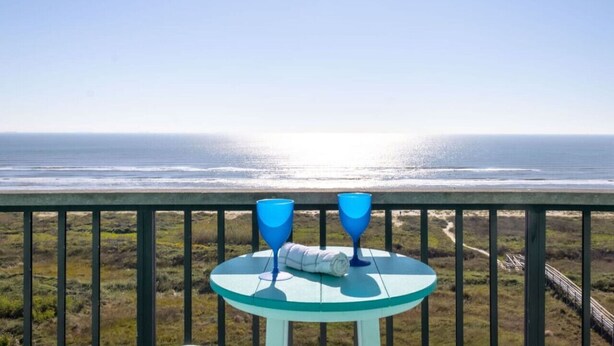A table with two blue glasses and a rolled towel on a balcony overlooking the ocean. - 911 Beachfront Heated Pool Gulf View 2 Bed 2 Bath (Galveston)