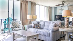 A living room with a striped sofa, two chairs, a table, and a TV. - 911 Beachfront Heated Pool Gulf View 2 Bed 2 Bath (Galveston)