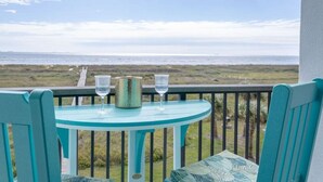 Une table et des chaises turquoise sur un balcon donnant sur une plage.