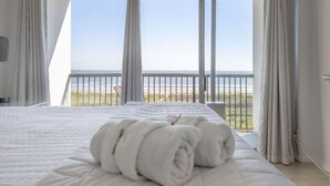 Ein Schlafzimmer mit einem Bett, weißen Handtüchern und einem Balkon mit Blick auf den Strand.