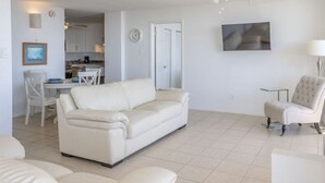 Ein geräumiges Wohnzimmer mit einem weißen Sofa, einem weißen Sessel und einem Essbereich mit Tisch und Stühlen.