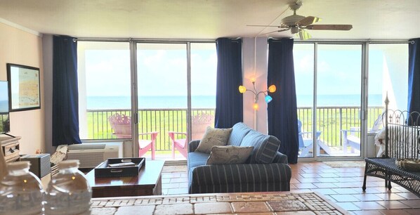 A living room with a sofa, a coffee table, and a view of the ocean through large sliding glass doors. - 212 Beachfront Heated Pool Gulf View XL Studio Loft (Galveston)