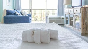 A neatly made bed with rolled white towels in the center, a blue sofa with cushions, and a rustic wooden cabinet with drawers. - 112 Heated pool, Gulf View (Galveston)