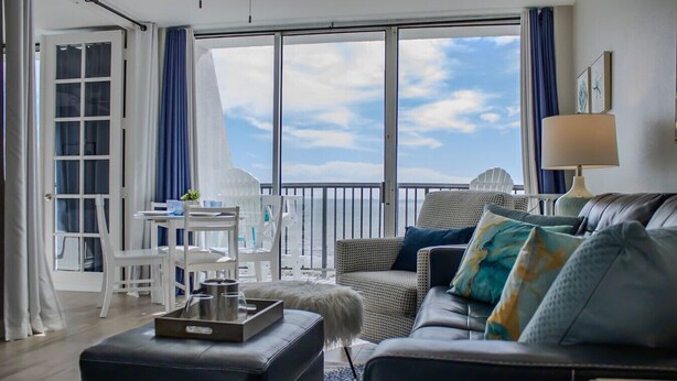 Una sala de estar moderna con balcón, muebles blancos y vista al cielo.