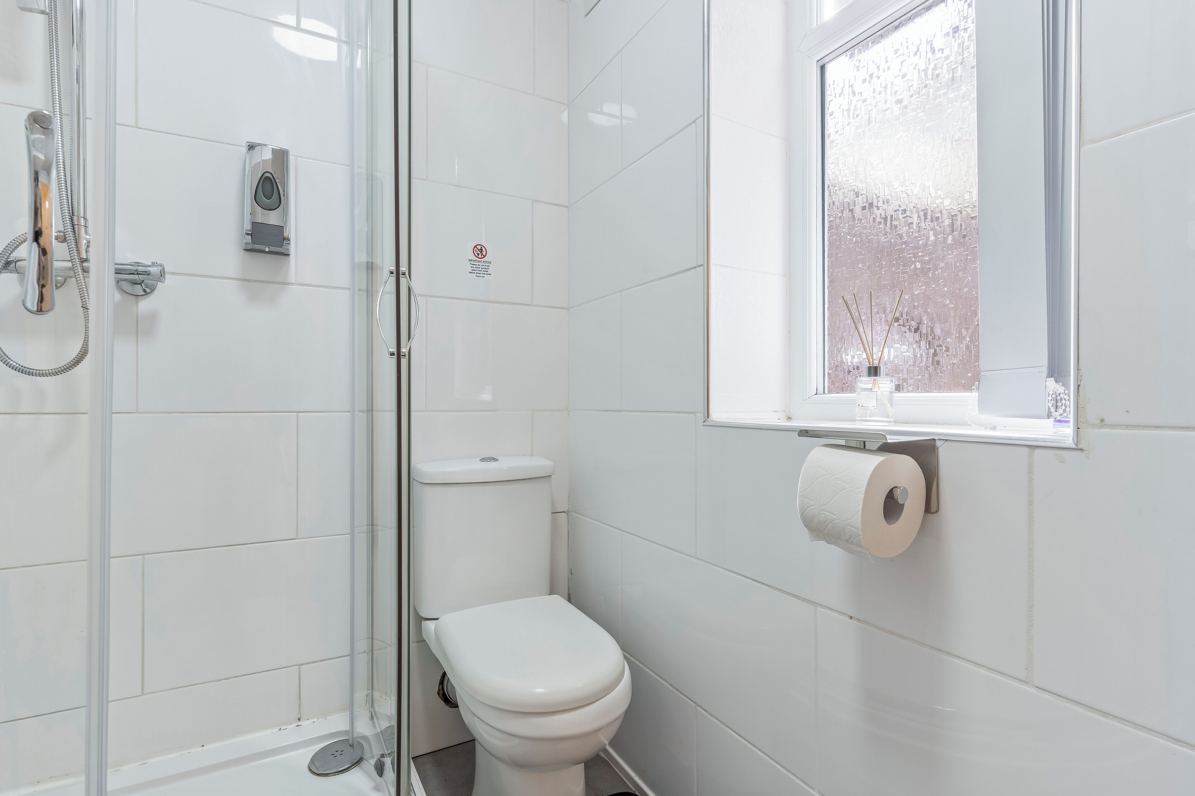 Egy fürdőszoba üveg válaszfallal ellátott zuhanyzóval, WC-vel és egy ablakkal, melyből a fákra nyílik kilátás.