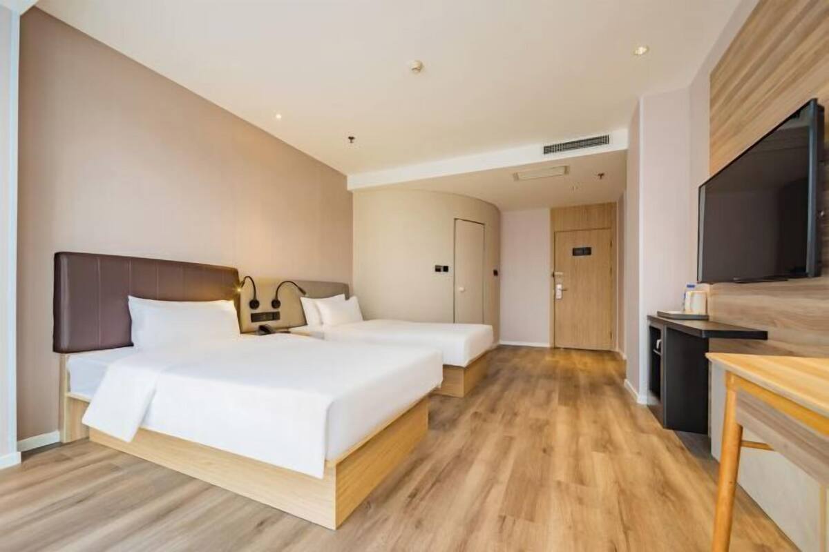 Ein Hotelzimmer mit zwei Betten, einem Fernseher, einem Schreibtisch und einer Tür zu einem weiteren Raum.