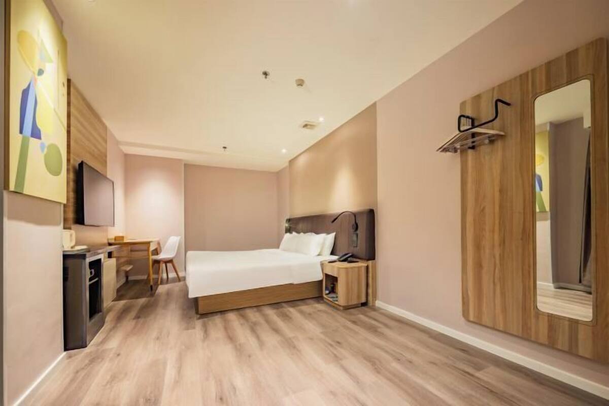Ein Hotelzimmer mit Bett, Nachttisch, Lampe, Fernseher und einem kleinen Schreibtisch mit Stuhl.
