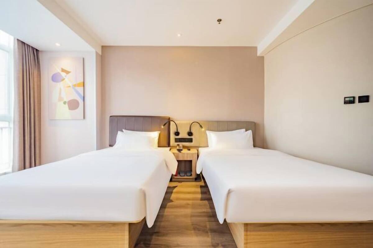 Ein Hotelzimmer mit zwei Betten, Holzboden, einer neutralen Farbgestaltung und einem an der Wand hängenden Kunstwerk.