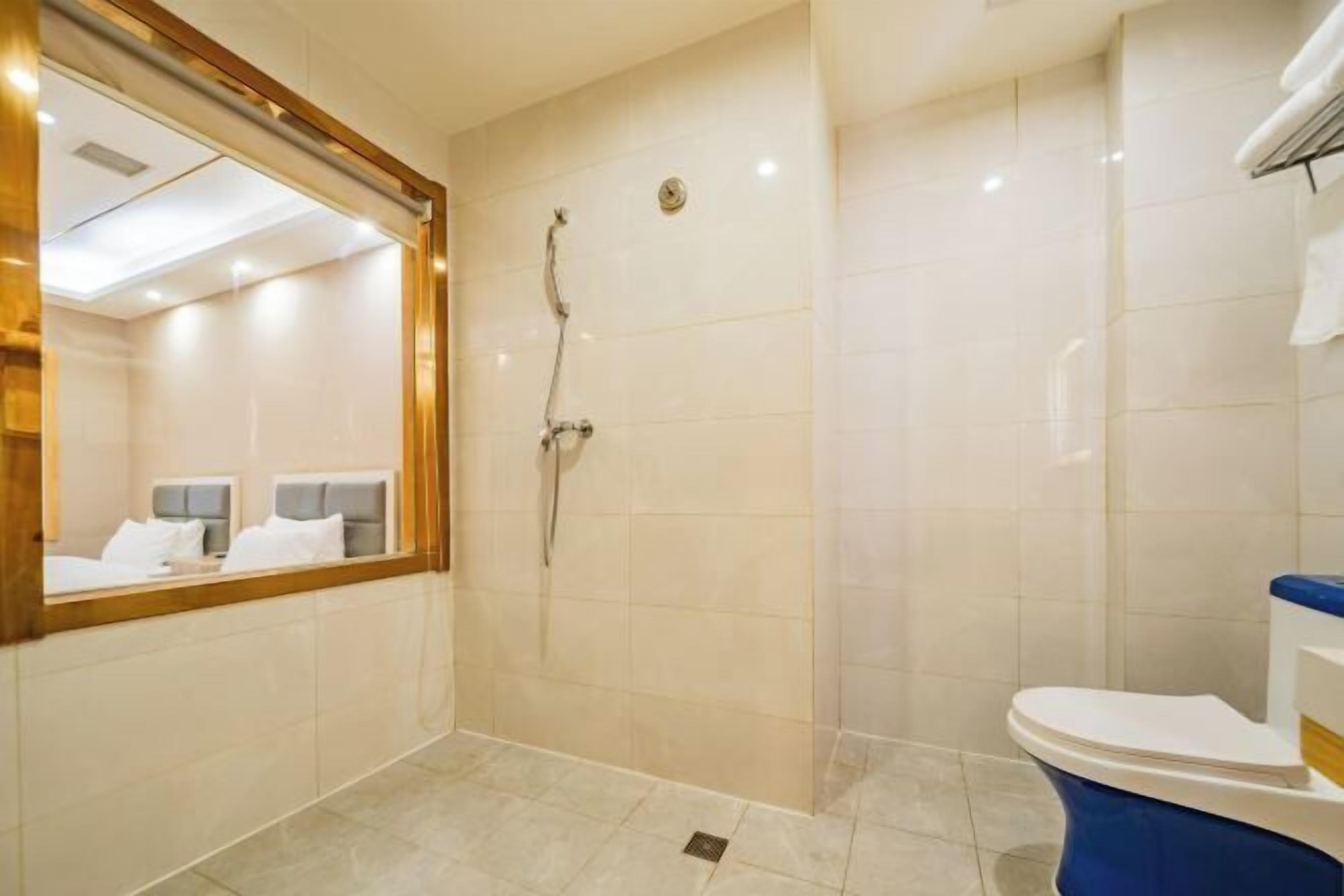 Une salle de bain d’hôtel équipée d’une douche, de toilettes et d’un miroir qui reflète un lit et une tête de lit.