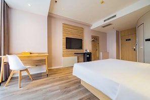 Habitación de hotel con cama, escritorio, silla, televisor y armario.