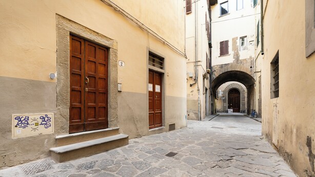 A narrow cobblestone street flanked by buildings with wooden doors and a stone staircase.