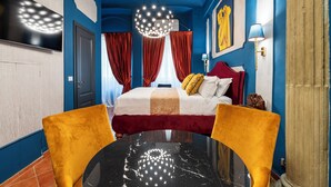 A bedroom with a bed, curtains, a chandelier, a TV, and a table.