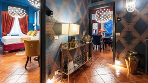 A hotel room with a bed, a vanity with a mirror, a chandelier, and a dining area with a table and chairs.
