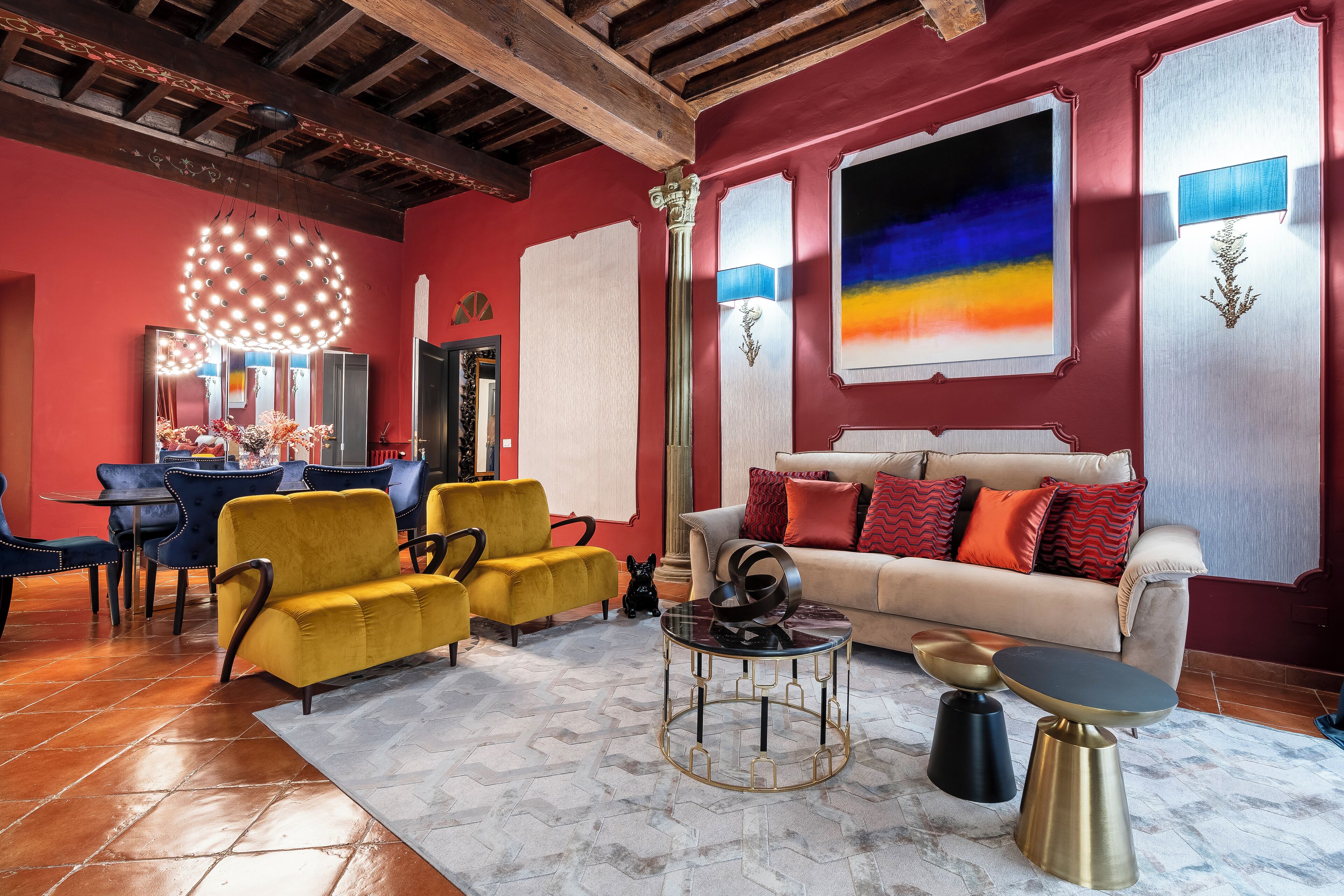 A living room with a red wall, yellow sofa, and a beige sofa with red cushions. There is a round coffee table with a black top and gold legs.