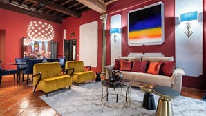 A living room with a red wall, yellow sofa, and a beige sofa with red cushions. There is a round coffee table with a black top and gold legs.