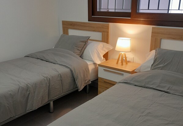 A twin room with two beds, a nightstand with a lamp, and a window above the beds. - Shuske - Private garden, swimming pool and... very close to the sea (Mar de pulpi)