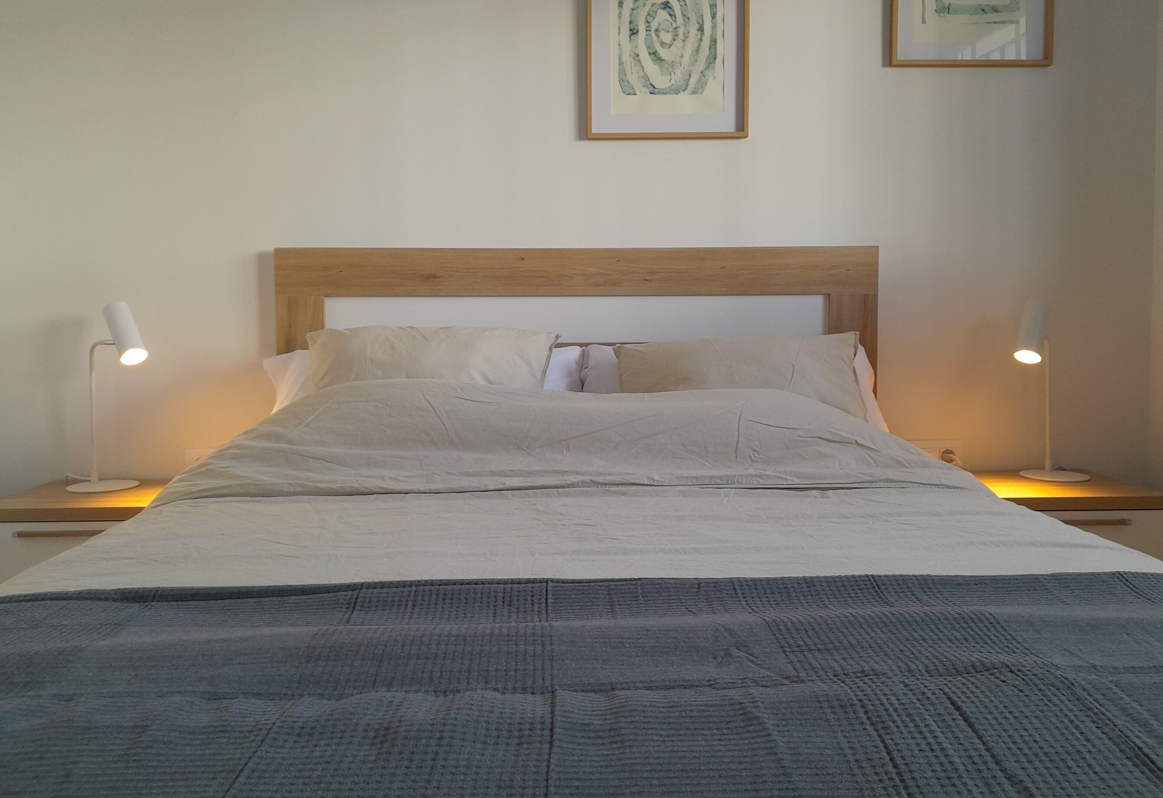 A neatly made bed with a wooden headboard, two bedside lamps, and a framed abstract artwork on the wall.