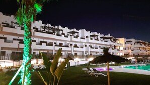 Ein Hotel mit Poolbereich, Liegestühlen und einer Palme mit grüner Beleuchtung.