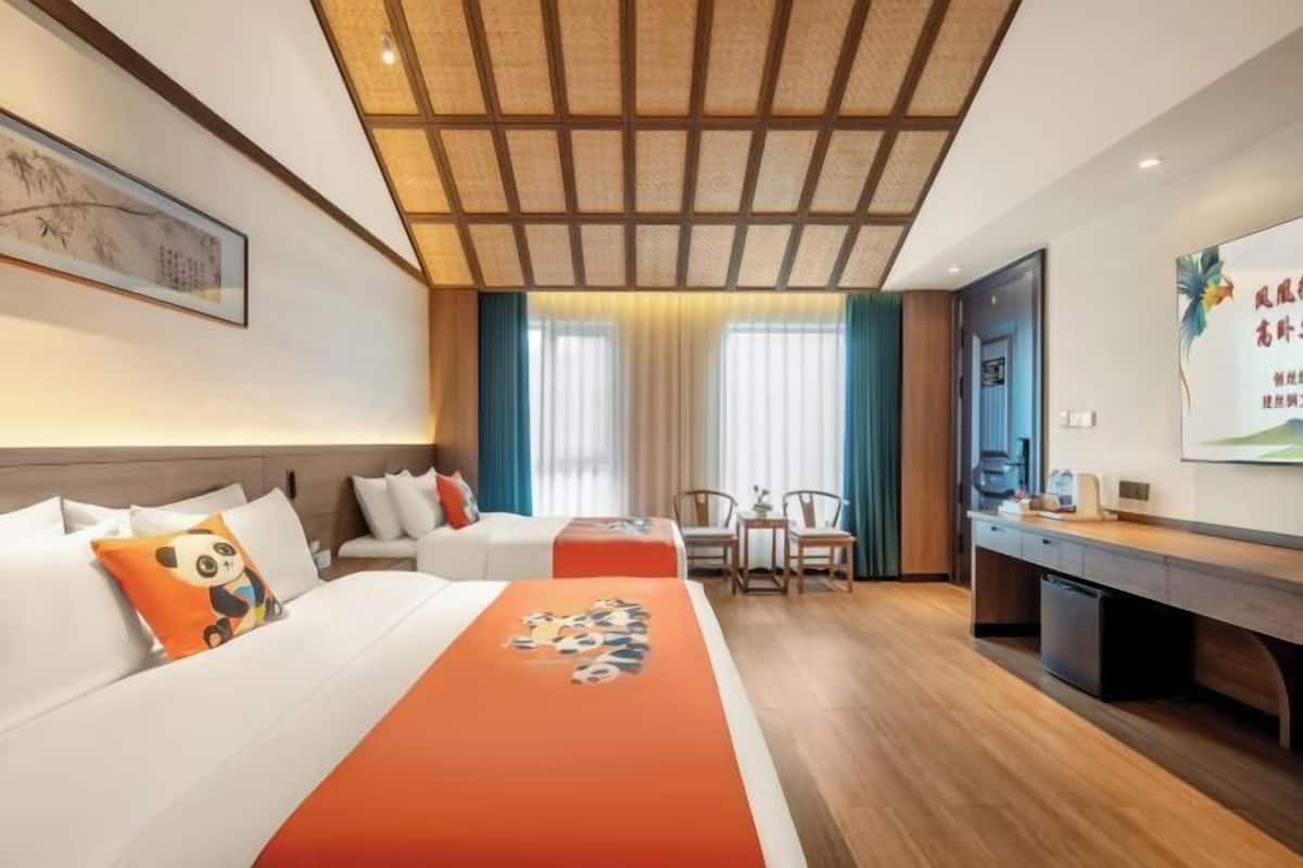 A hotel room with a bed, two chairs, a desk, and a television.