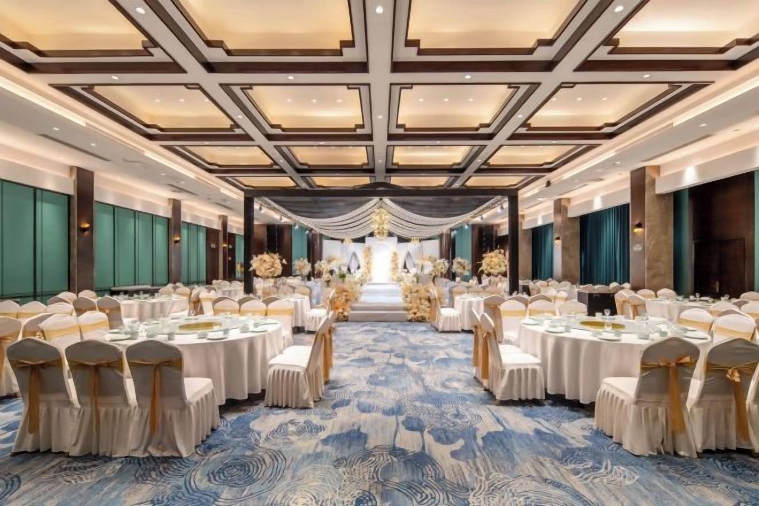 A banquet hall with round tables, white chairs, and a blue carpet.