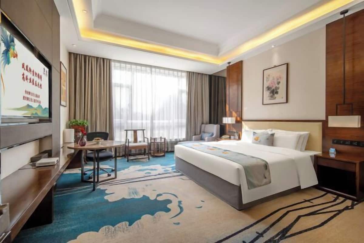 A hotel room with a bed, desk, chair, TV, and curtains.
