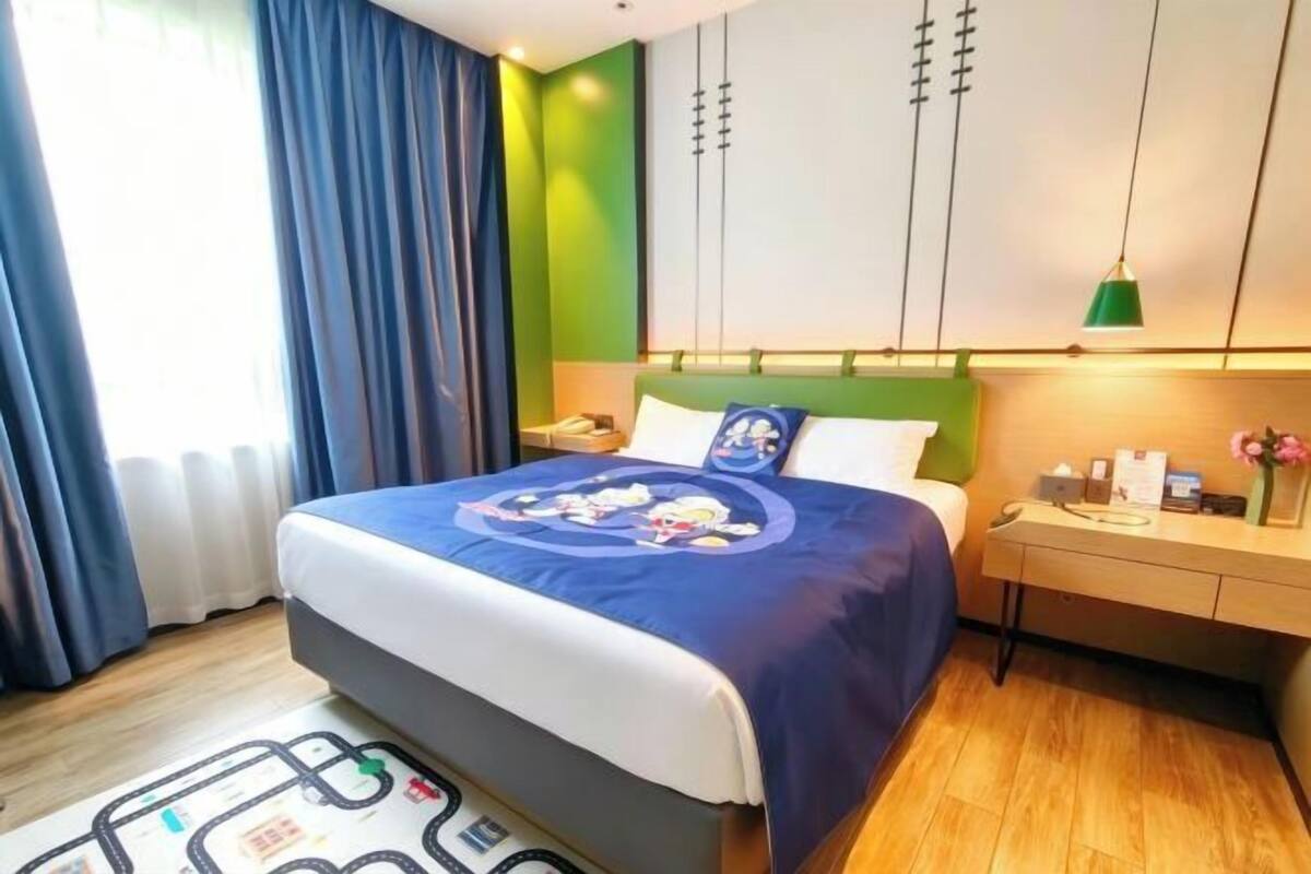 A hotel room with a bed, a nightstand, a desk, and a window with curtains.