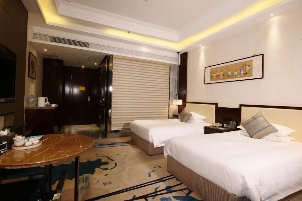 A hotel room with two beds, a dining table, a TV, and a painting on the wall.