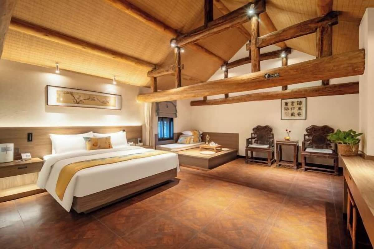 A spacious bedroom with a large bed, wooden beams, a bedside table, a small table, and a chair.