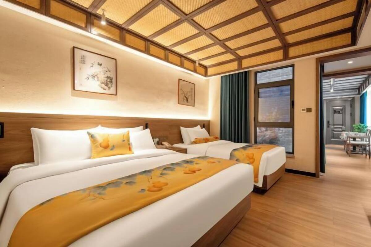 A hotel room with two beds, a wooden ceiling, artwork on the walls, and a view through a glass door.