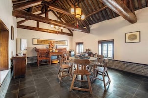 Una habitación amplia con techo alto, vigas de madera a la vista, una mesa redonda de comedor con sillas y una chimenea.