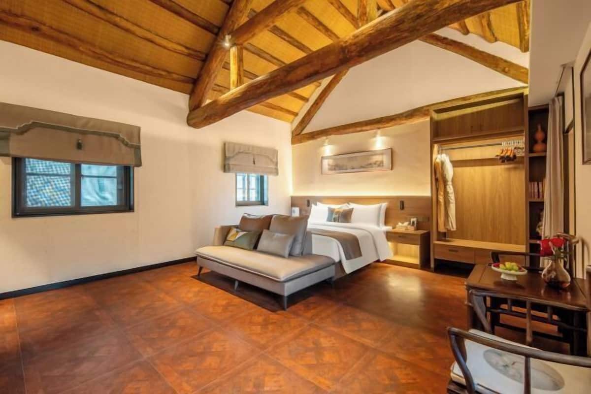 A bedroom with a wooden ceiling, a sofa, a bed, a nightstand, and a wardrobe.
