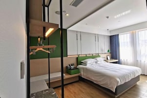 Una habitación de hotel moderna con cama, mesitas de noche, una pared de acento verde y un gran ventanal con cortinas.