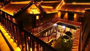 A traditional building with a tiled roof and wooden railings, featuring a central courtyard with a staircase leading to an upper level. - Zhouchun Hotel (Zibo)